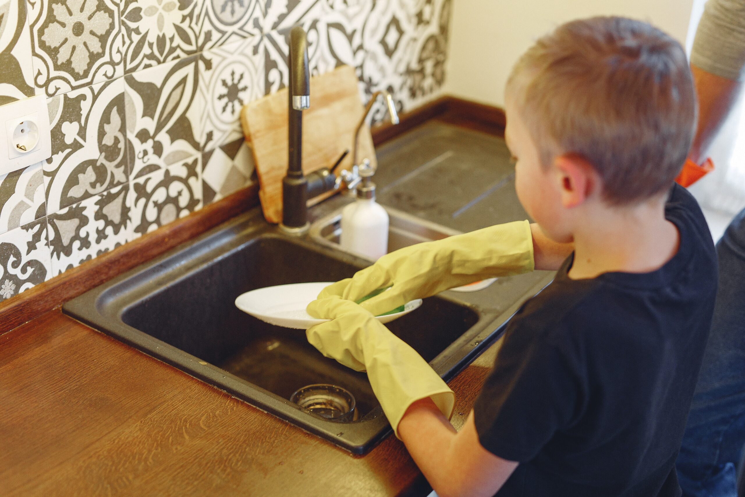 A boy in a black t-shirt is washing dishes