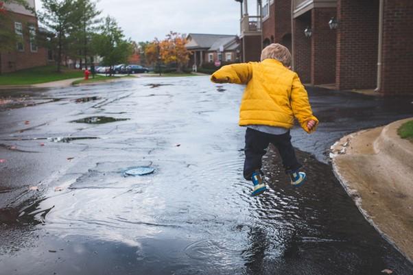 Toddler in yellow coat jumping in puddles