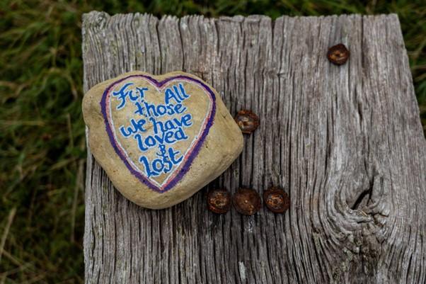 A rock on a tree with an engraved message ‘for all those we have loved & lost’