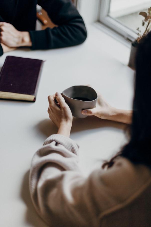 A photo of a woman holding a coffee and someone sitting opposite her